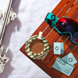 A HOJI BLANCA 30 PACK by Hoji sits on a wooden table beside ski goggles, two tea sachets, and single-serve olive oil packets, with skis nearby—all surrounded by snow.