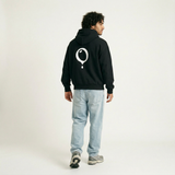 A man stands facing away in the Hoji HOJI HOODIE by Hoji, featuring an oversized fit and a large white balloon graphic on the back, paired with light blue jeans and gray sneakers against a plain light background.