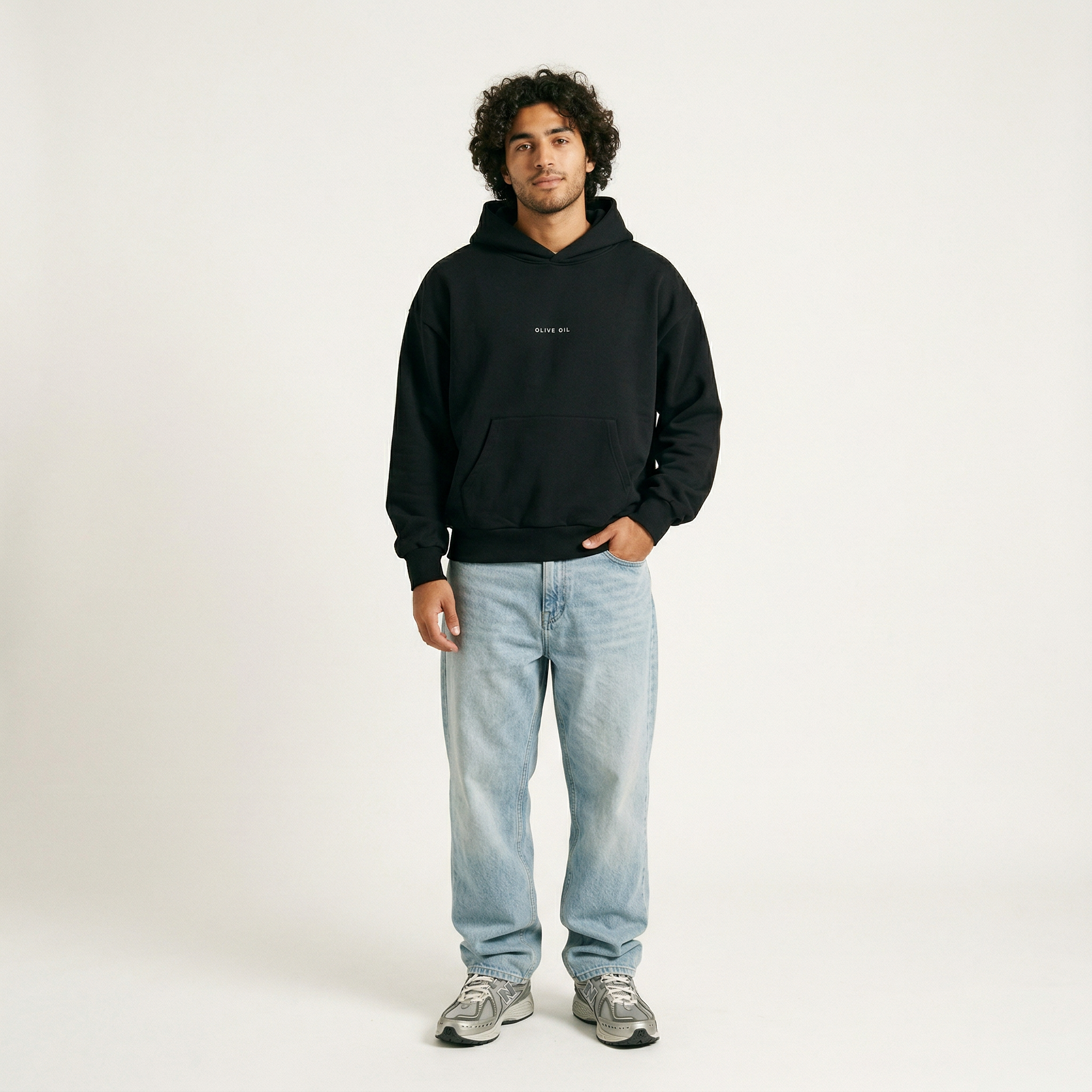 A young man with curly hair faces forward in a Hoji HOJI HOODIE, paired with light blue jeans and gray sneakers, set against a plain white background.