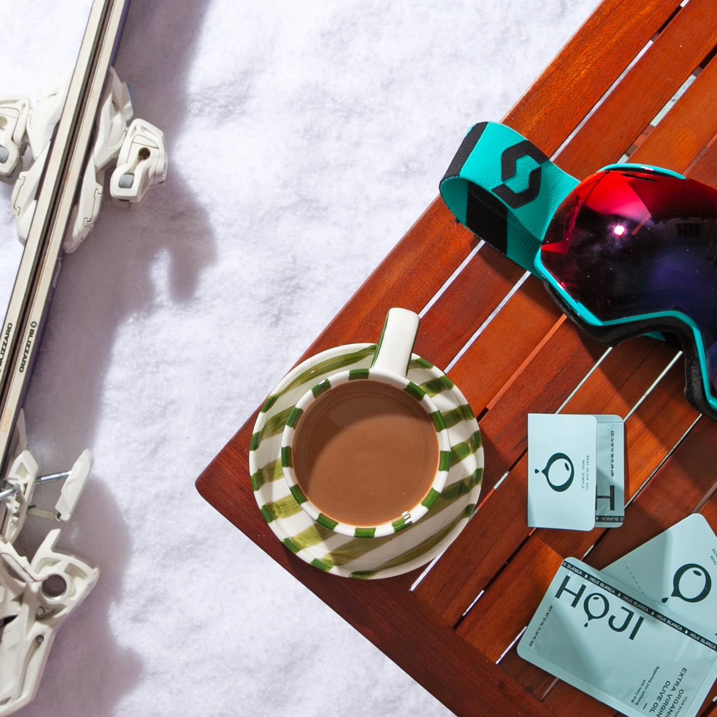 Ski equipment with a cup of coffee and goggles on a wooden table in the snow
